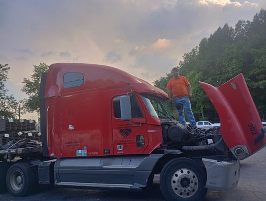 ATL Mobile Mechanics — Joseph on top of a red commercial semi-truck cab with the hood up, performing engine repair in the parking lot