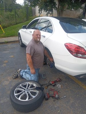 ATL Mobile Mechanics — Joseph kneeling beside a white sedan performing a mobile tire change with tools spread on the ground
